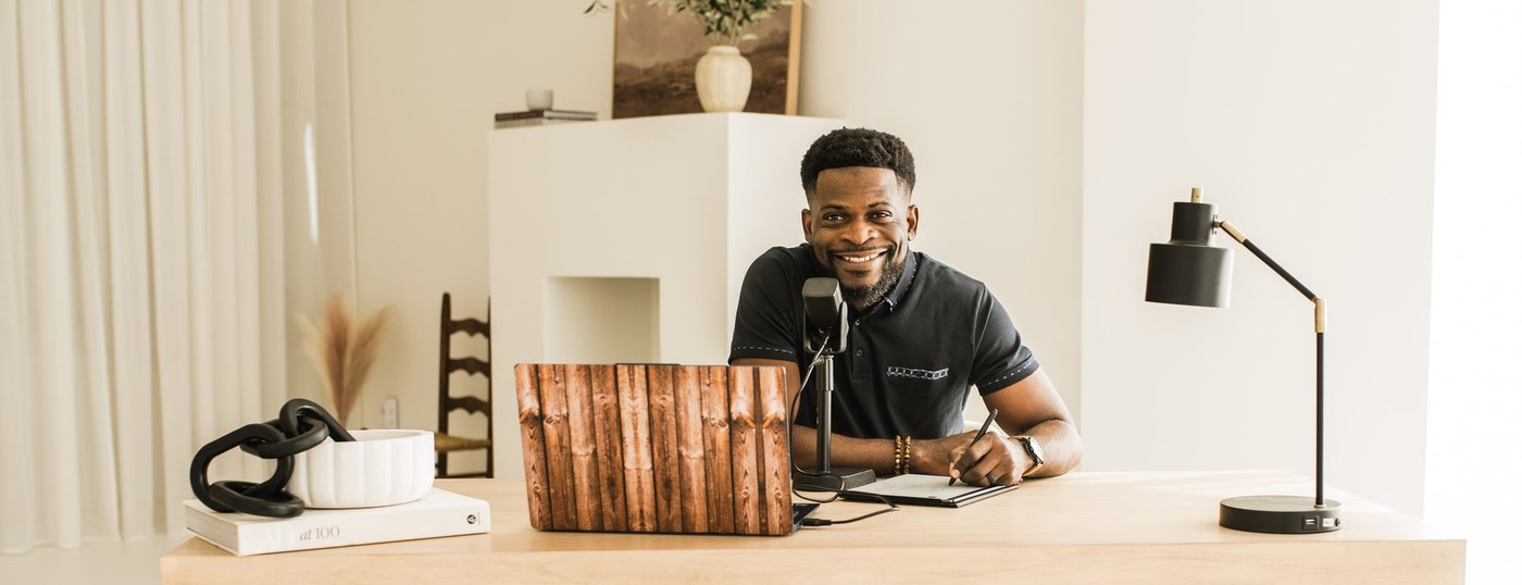 Seun Adeyemi at his desk with a microphone and notebook